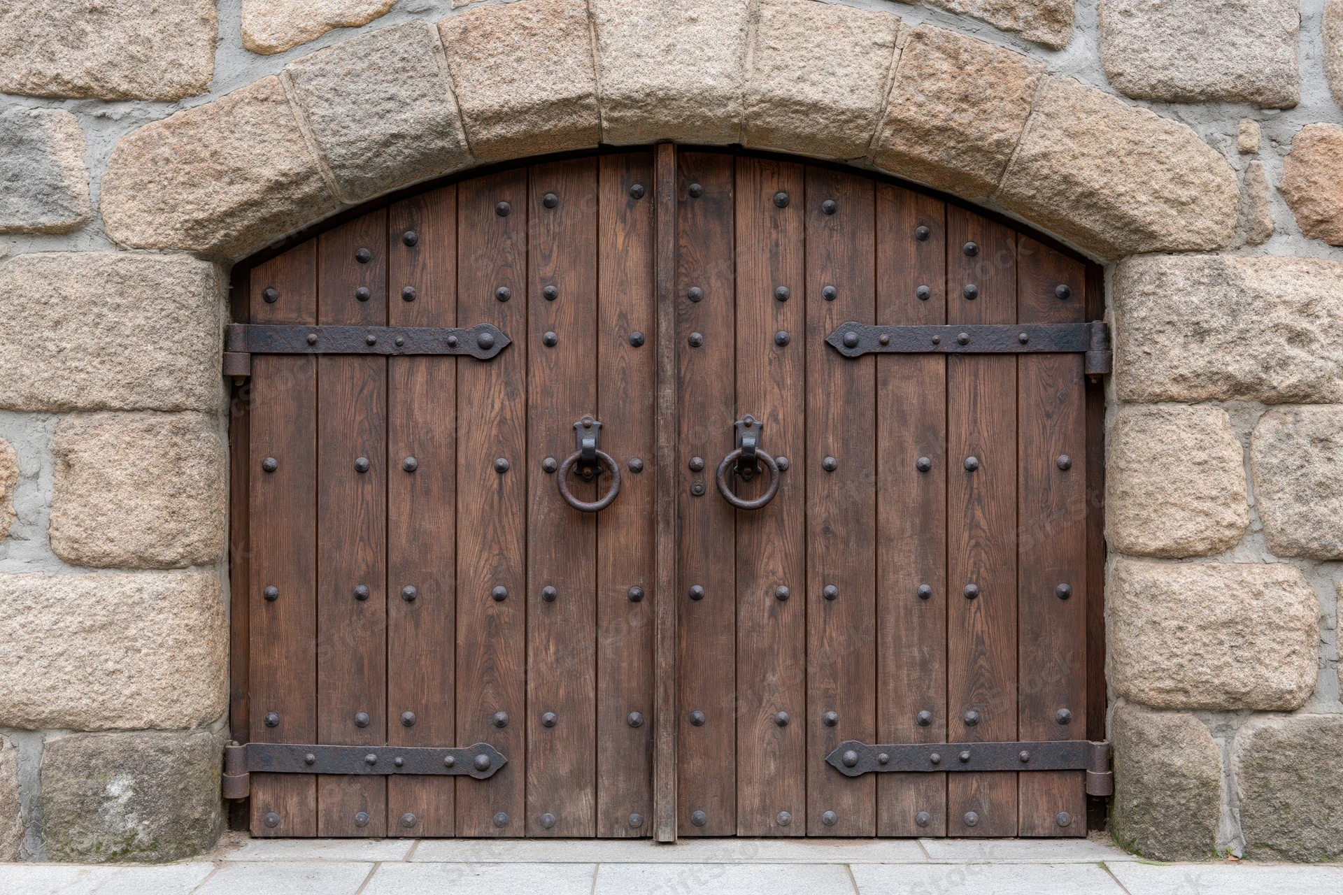 Arched double wooden door with iron hardware set in stone wall