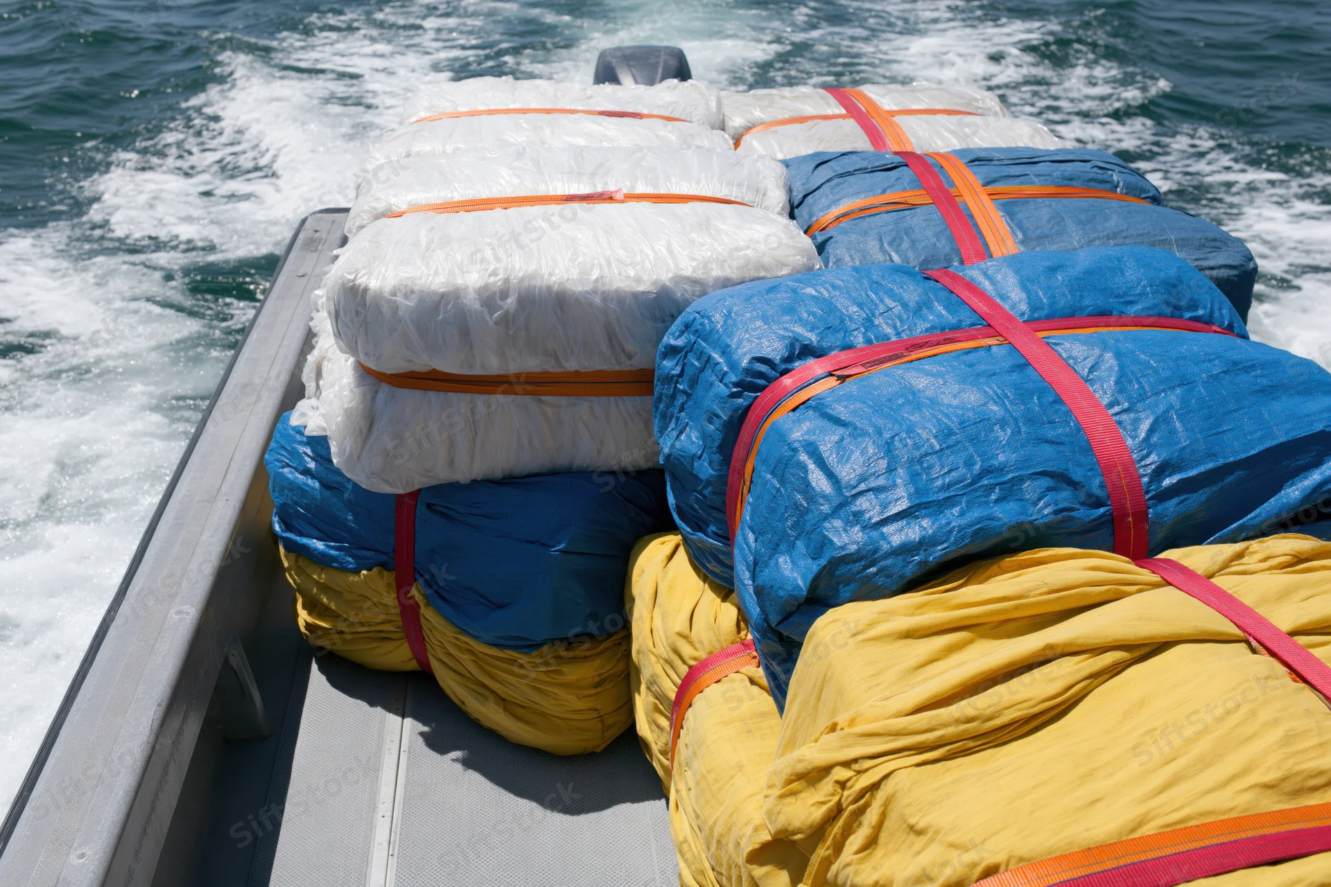 Stacked bales of wrapped packages secured with straps on a moving boat in the ocean