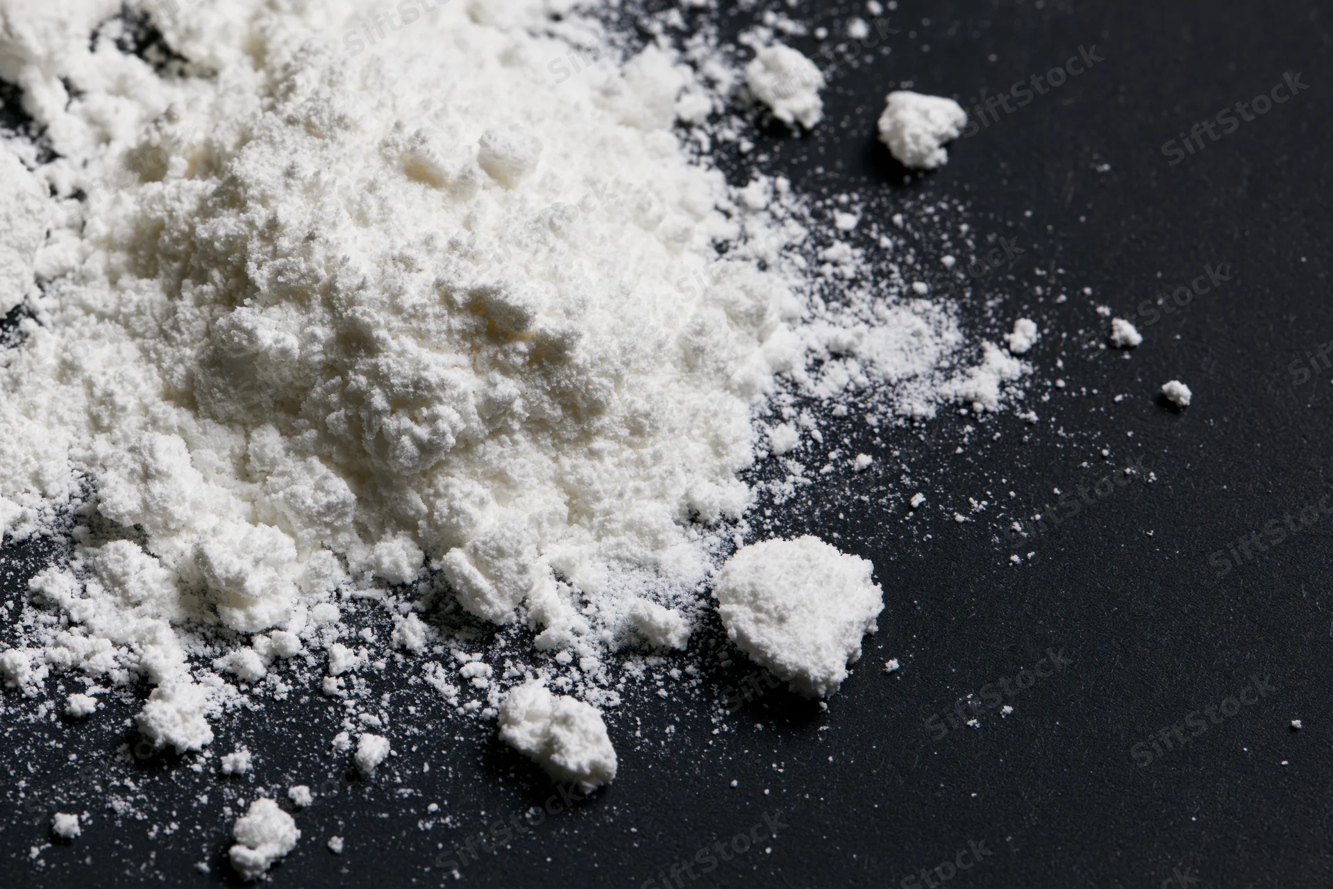 White powder scattered and spilled across a flat black surface