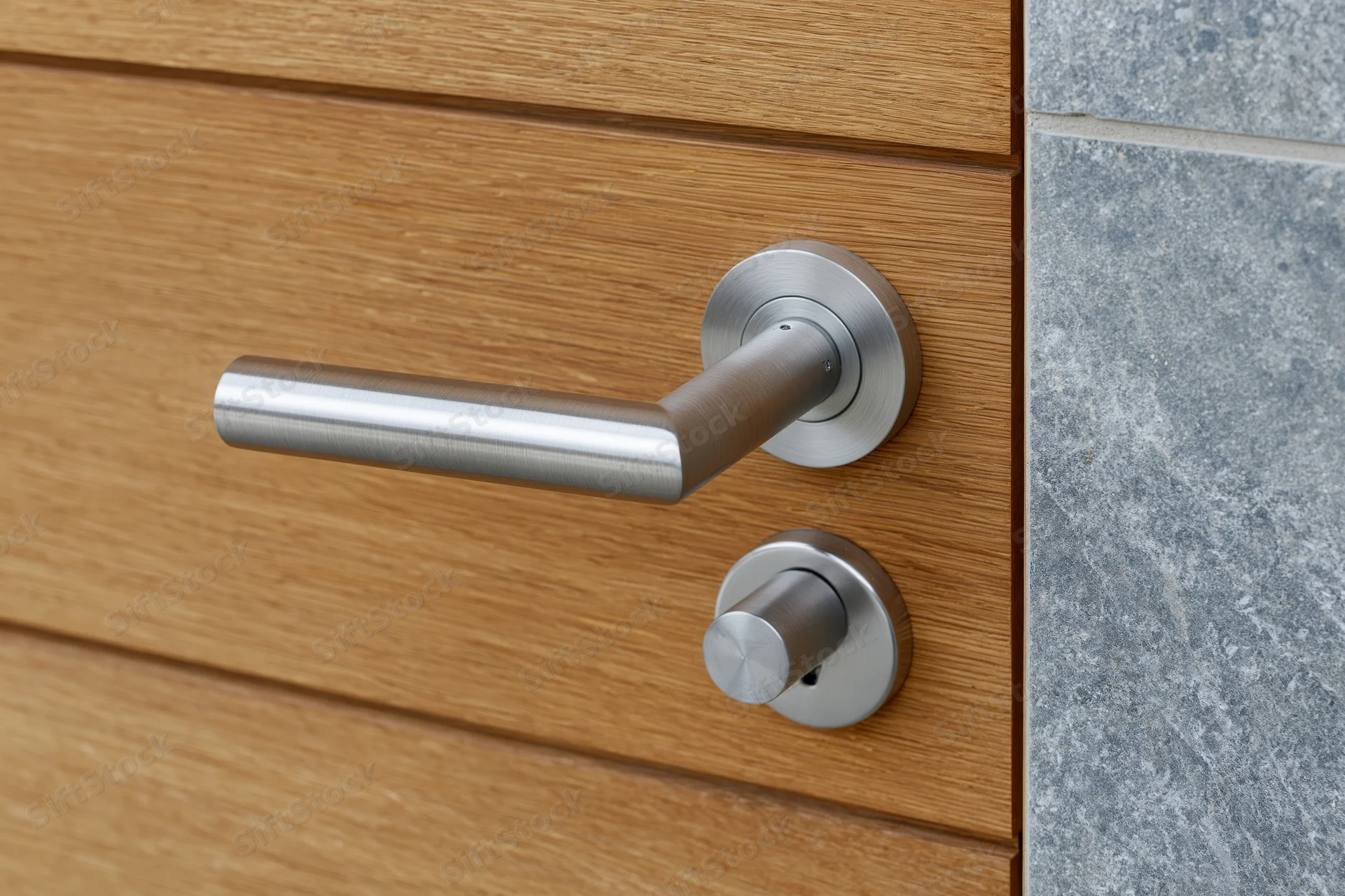 Modern brushed stainless steel lever door handle on a wooden door with stone siding