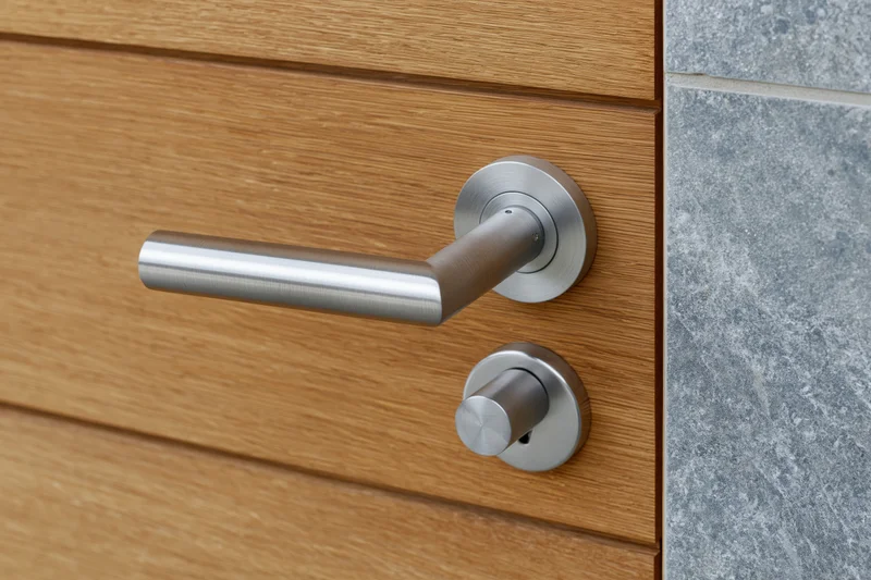 Modern brushed stainless steel lever door handle on a wooden door with stone siding