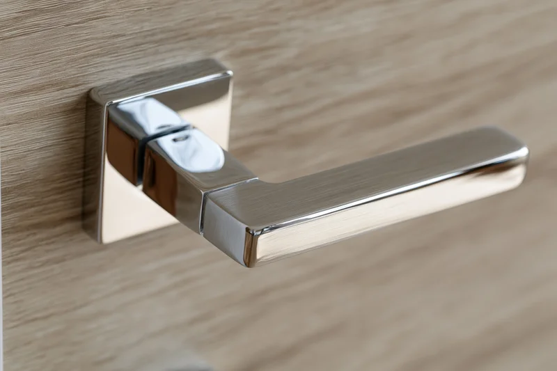 Modern chrome lever door handle with square backplate mounted on wooden door