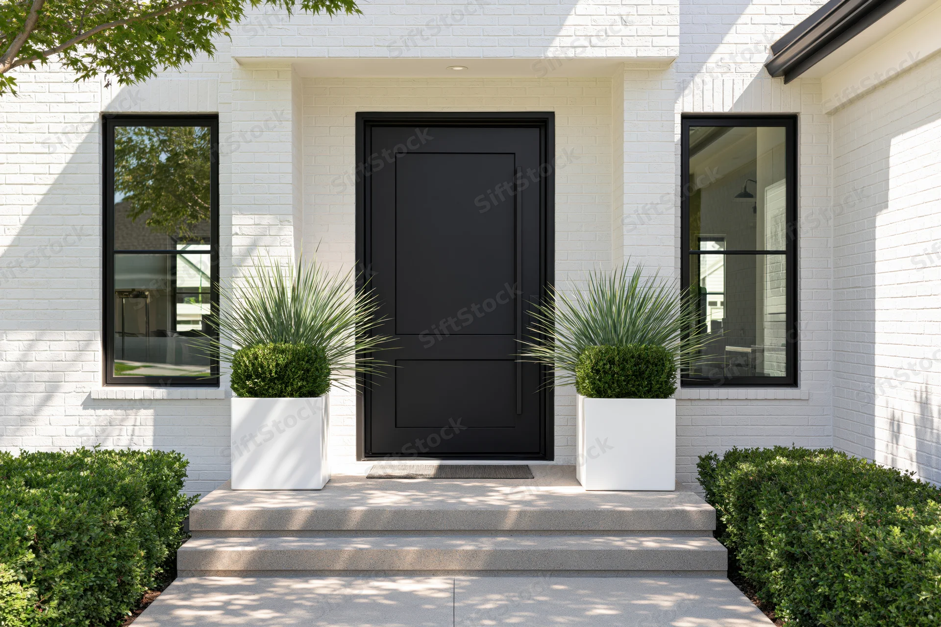 Modern home entrance with matte black pivot door flanked by white planters and greenery on a brick facade