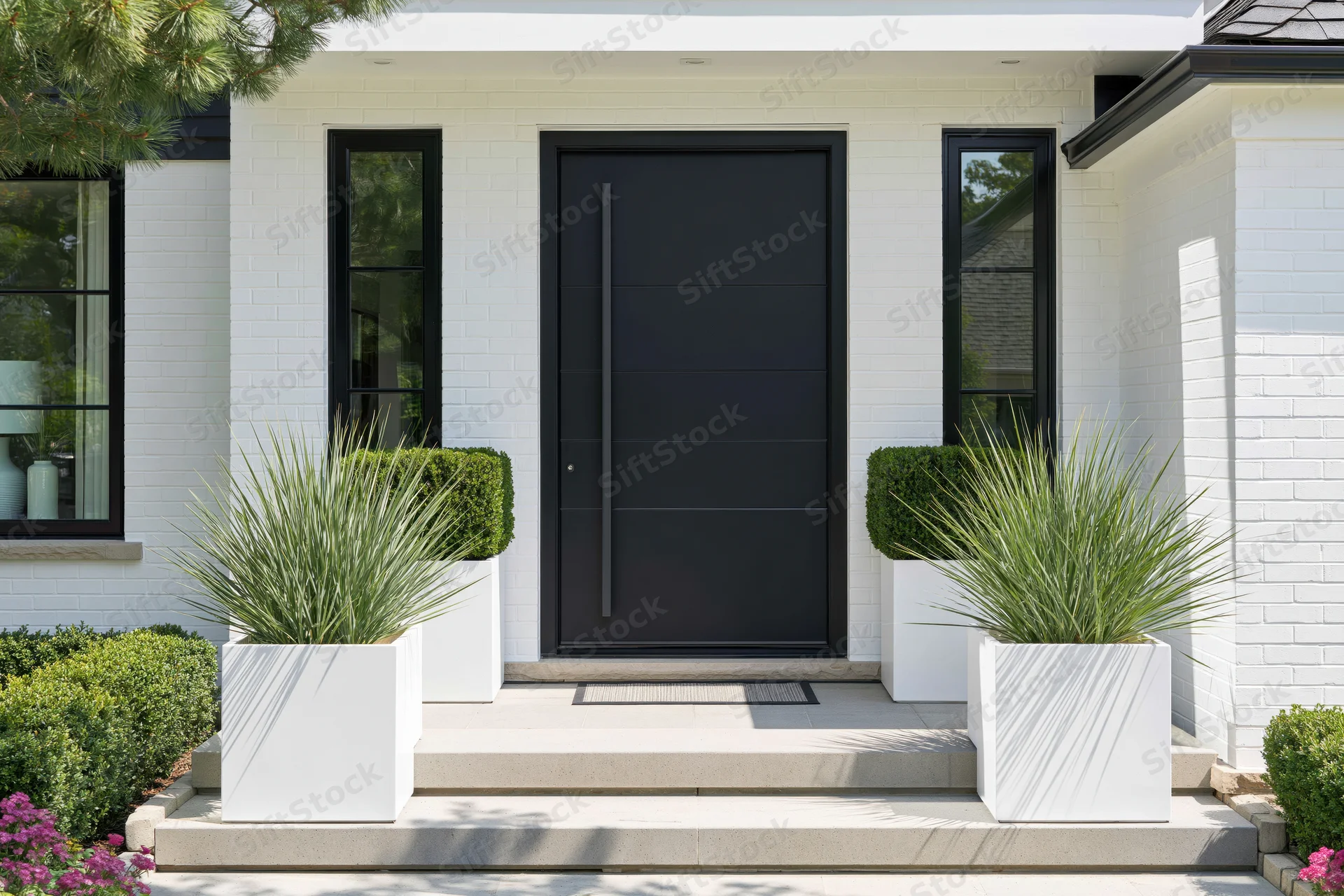 Modern home entrance with matte black pivot door flanked by white planters and greenery on a white brick facade