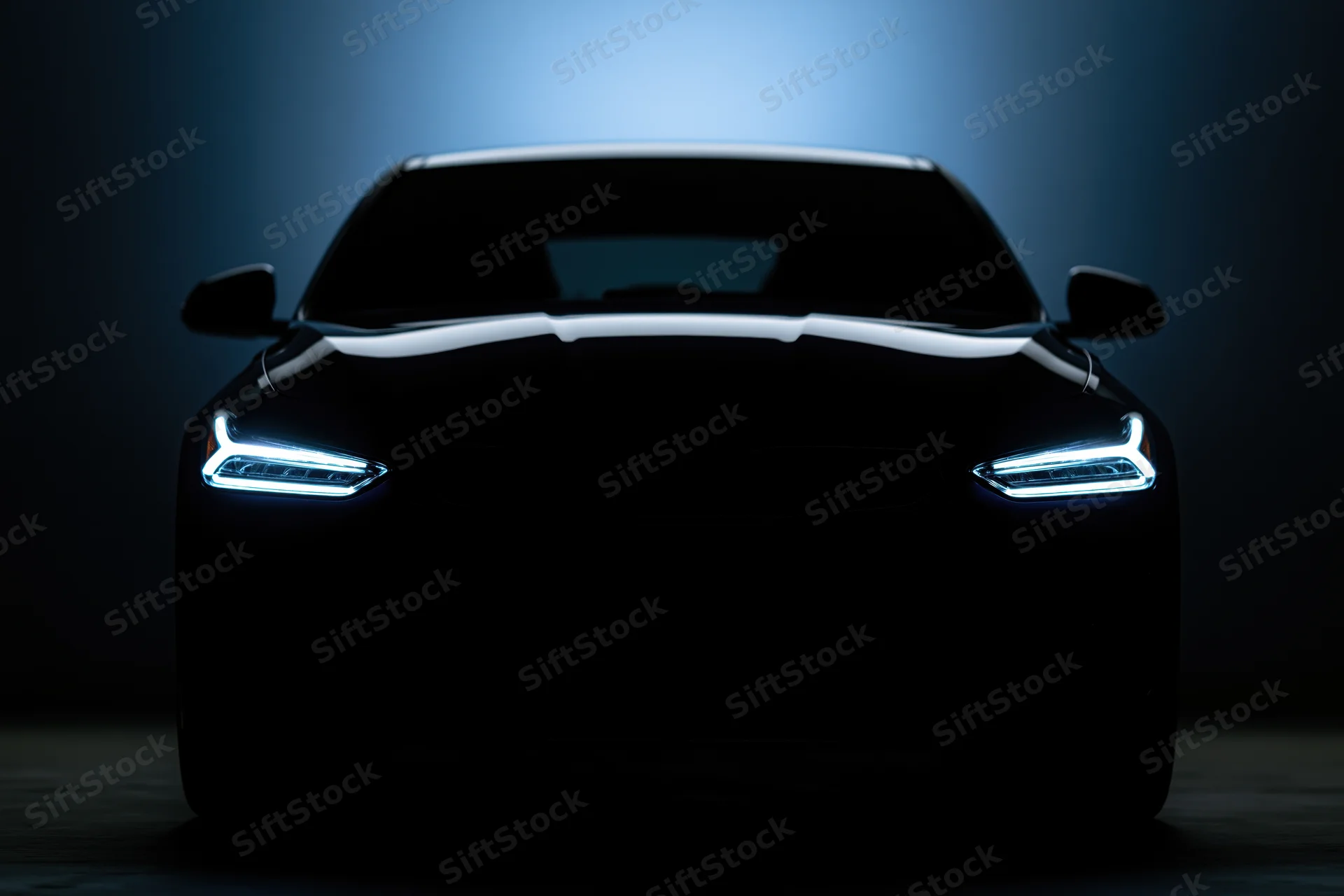 Modern sedan silhouetted head-on in dark studio with glowing led headlights