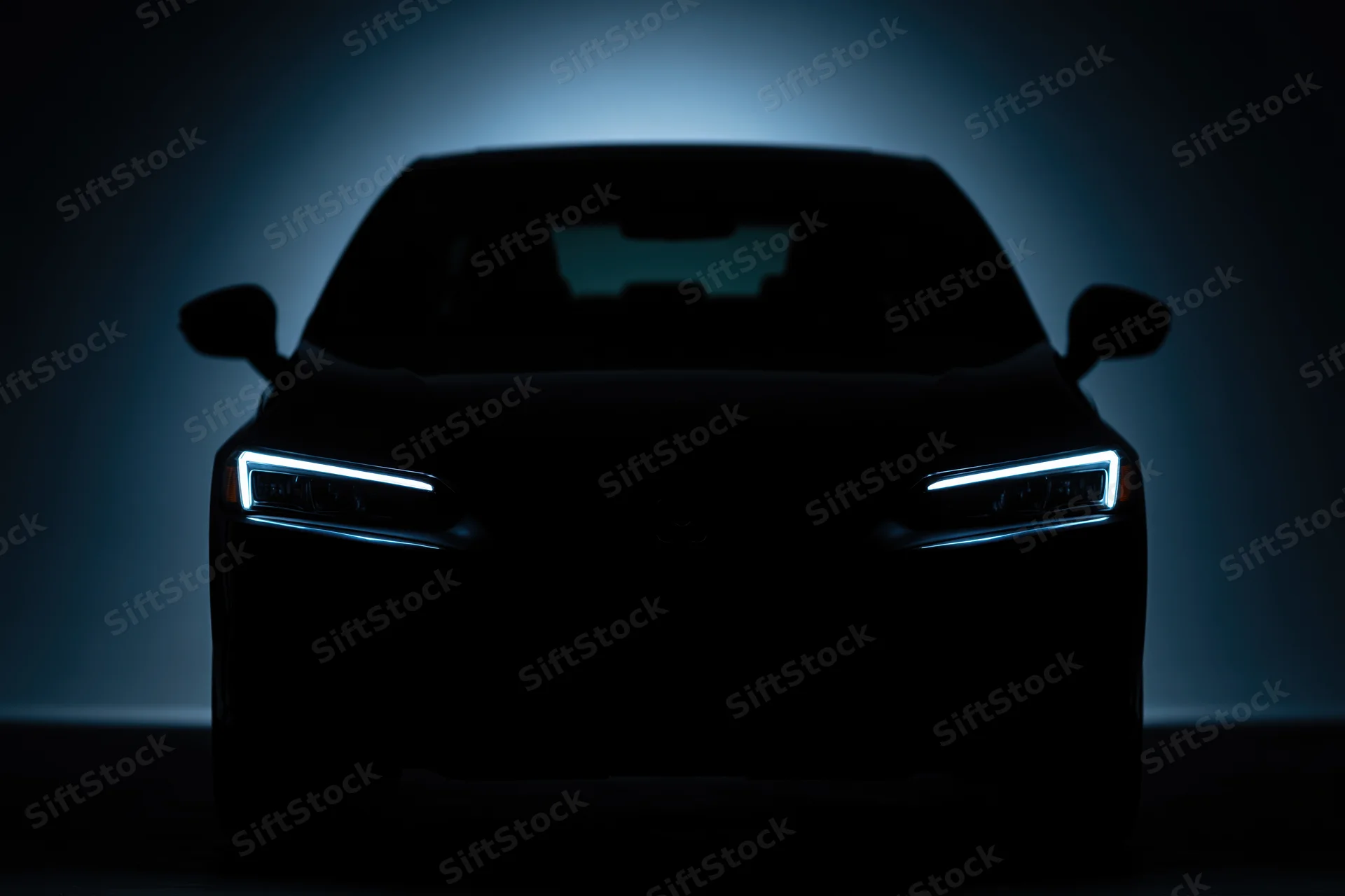 Modern sedan silhouetted head-on in near-total darkness with illuminated headlights