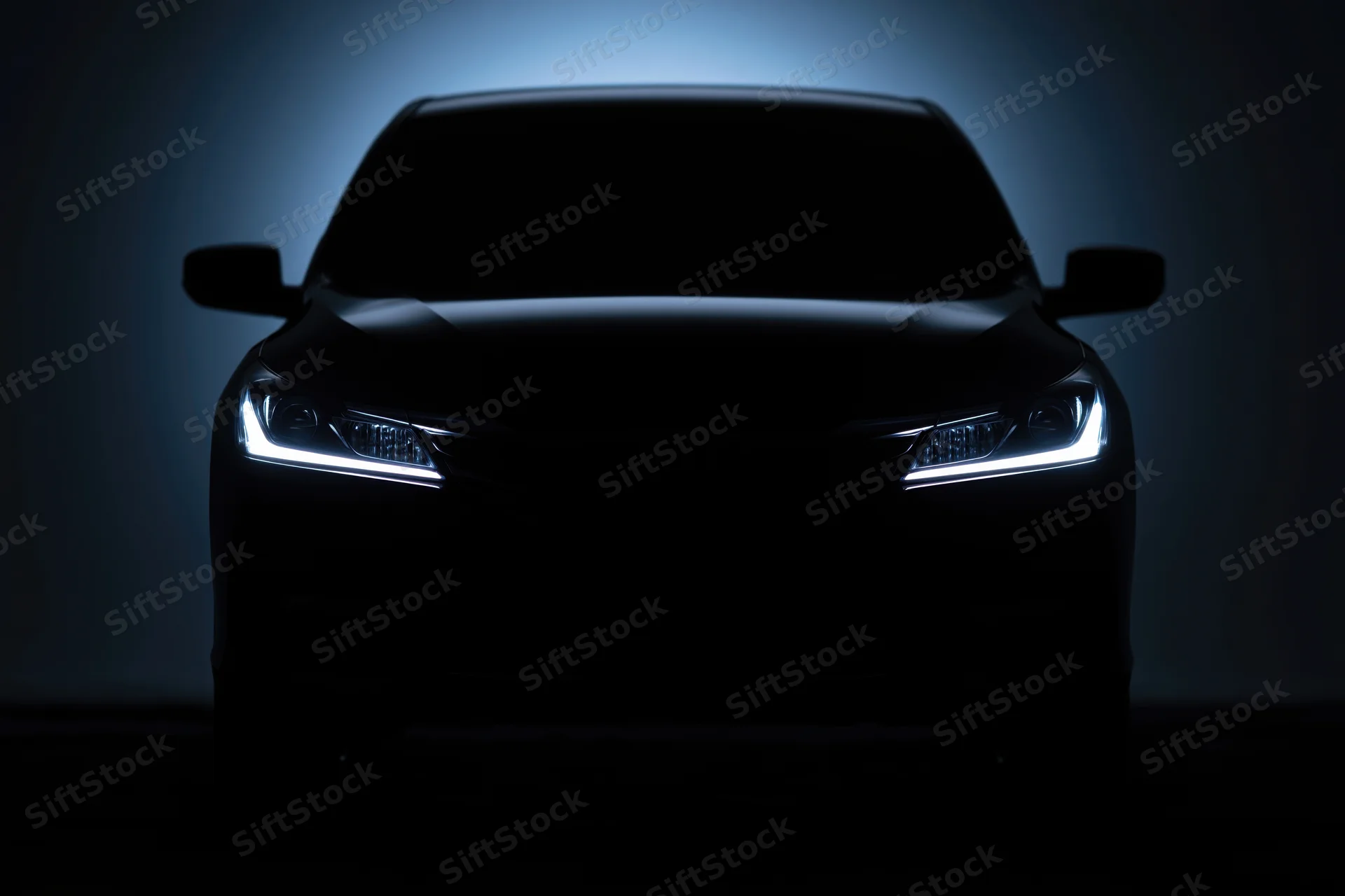 Modern sedan silhouetted head-on with illuminated headlights in dark studio setting