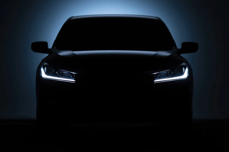 Modern sedan silhouetted head-on with illuminated headlights in dark studio setting