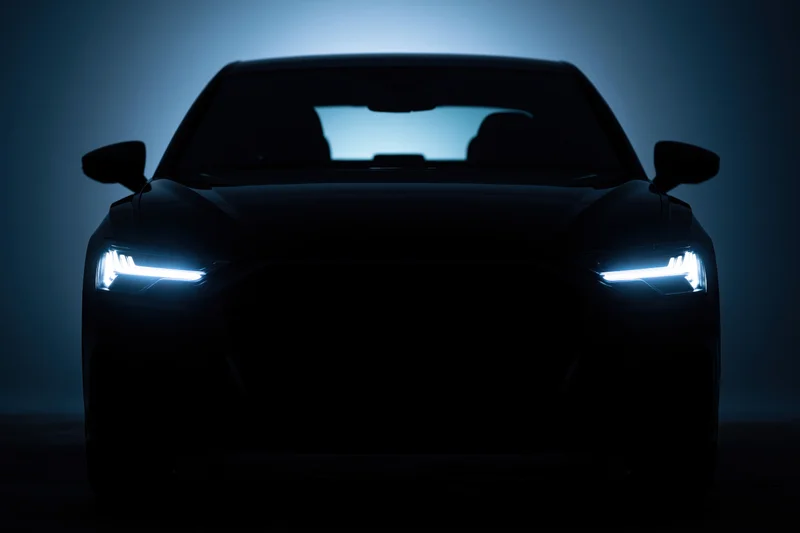 Modern sedan silhouetted head-on in dark studio with glowing led headlights