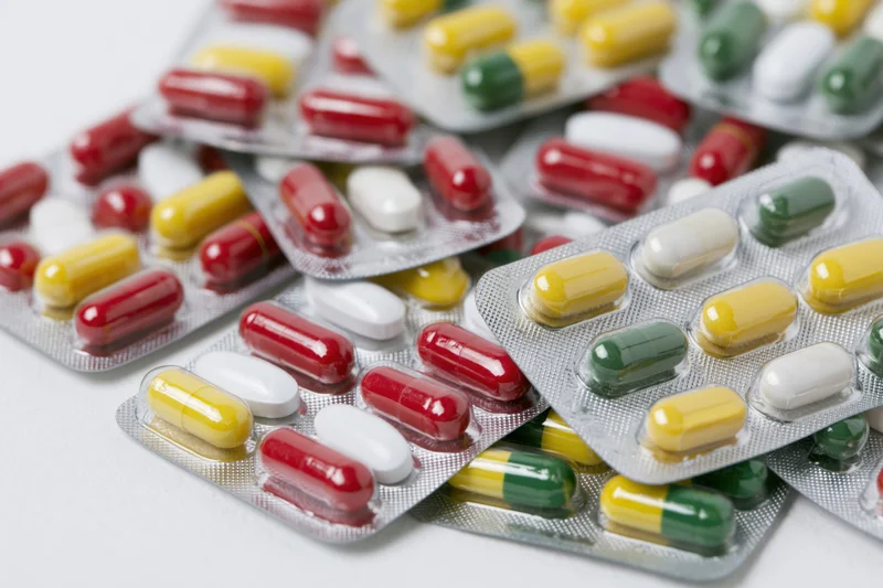 Scattered pharmaceutical blister packs with colorful capsules and tablets on white surface
