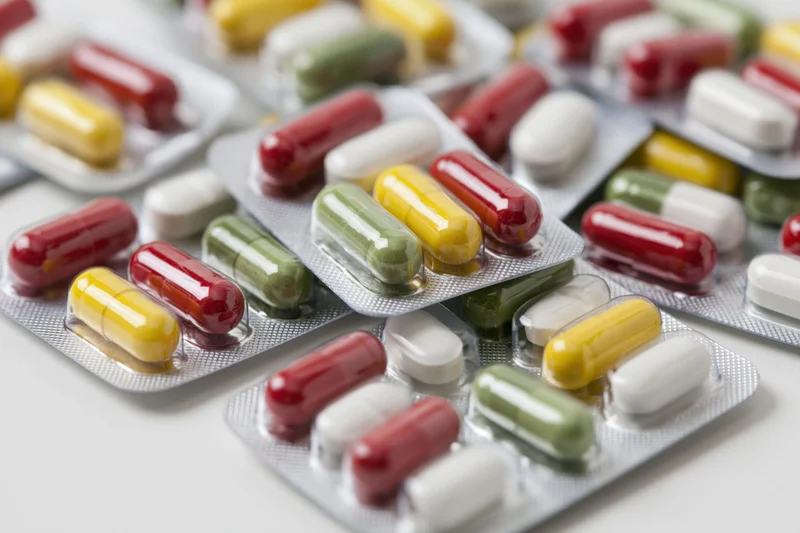 Scattered pharmaceutical blister packs with colorful capsules and tablets on a white surface