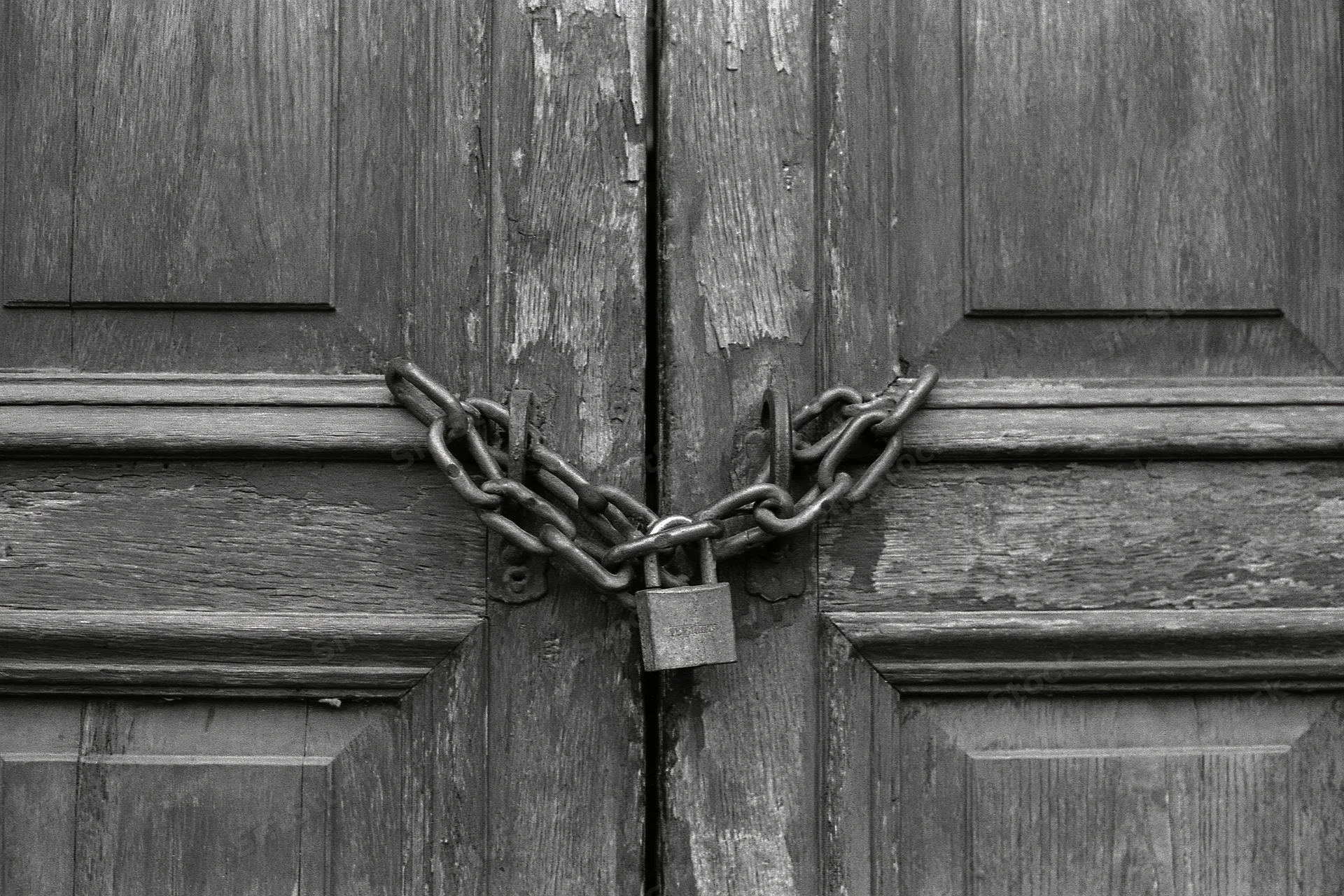 Weathered wooden double doors secured with a heavy chain and padlock at the center