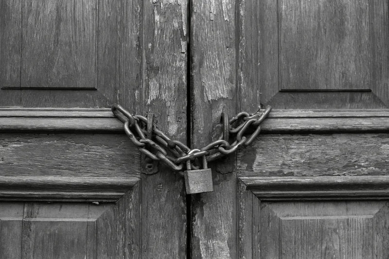 Weathered wooden double doors secured with a heavy chain and padlock at the center