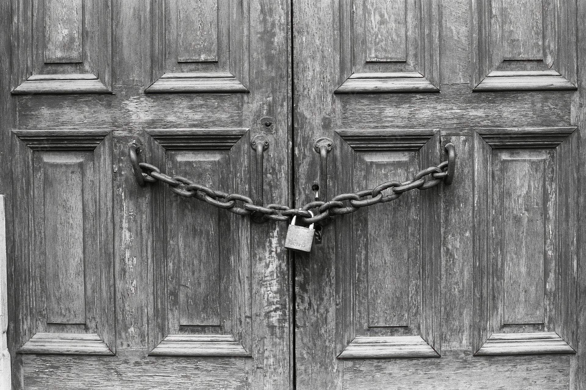Weathered wooden double doors secured with a heavy chain and padlock at the center