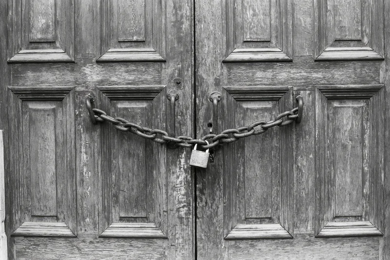 Weathered wooden double doors secured with a heavy chain and padlock at the center
