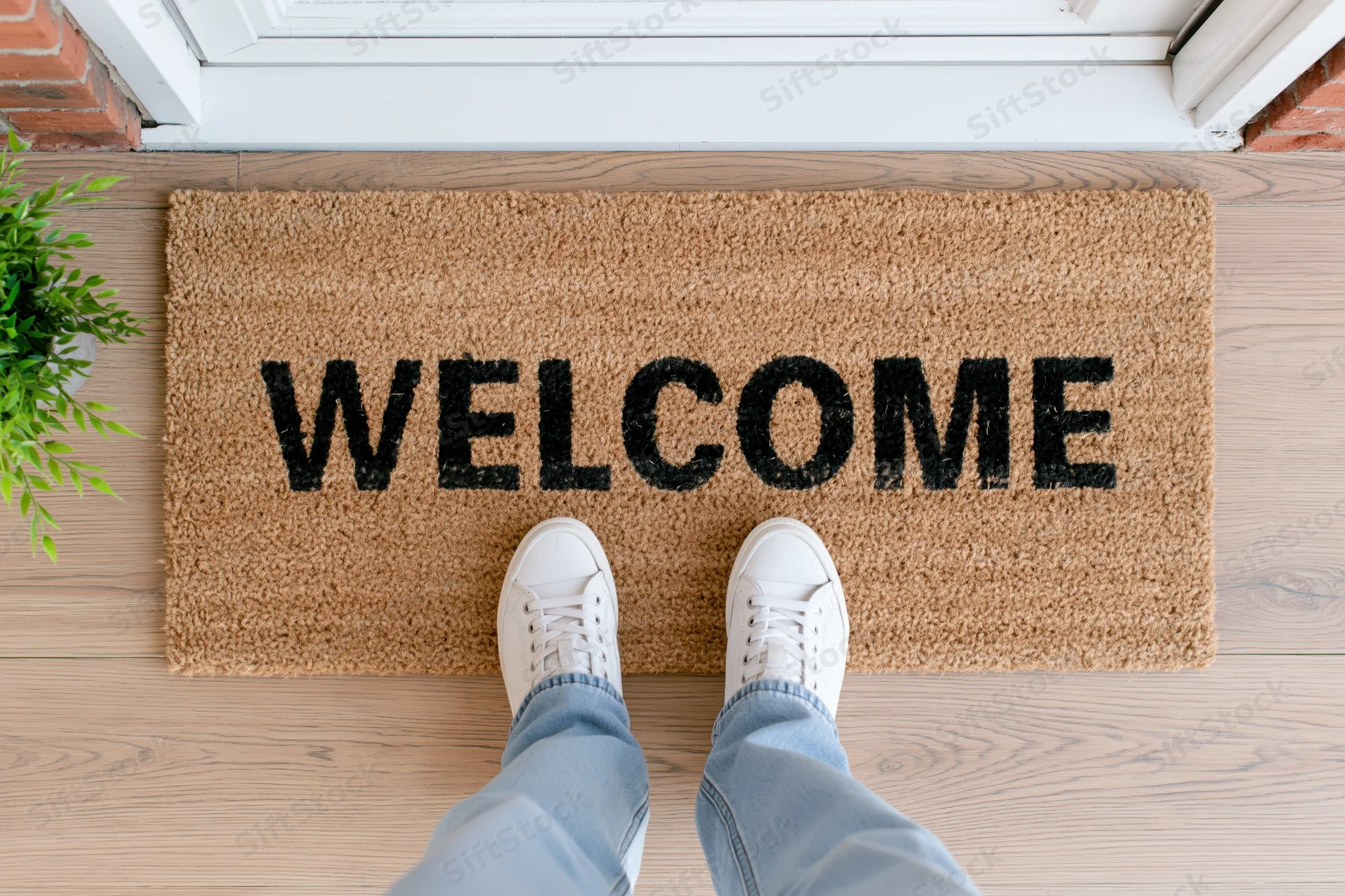 Feet in white sneakers standing on a welcome doormat at a house entrance