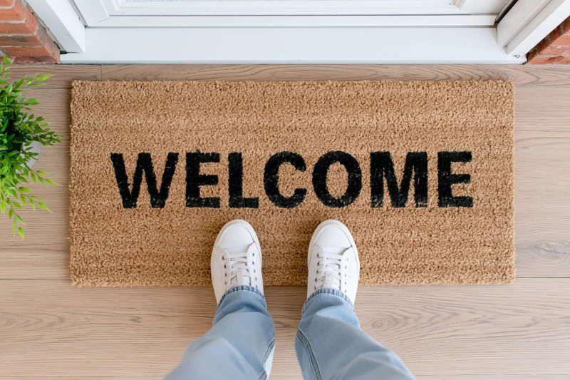 Feet in white sneakers standing on a welcome doormat at a house entrance