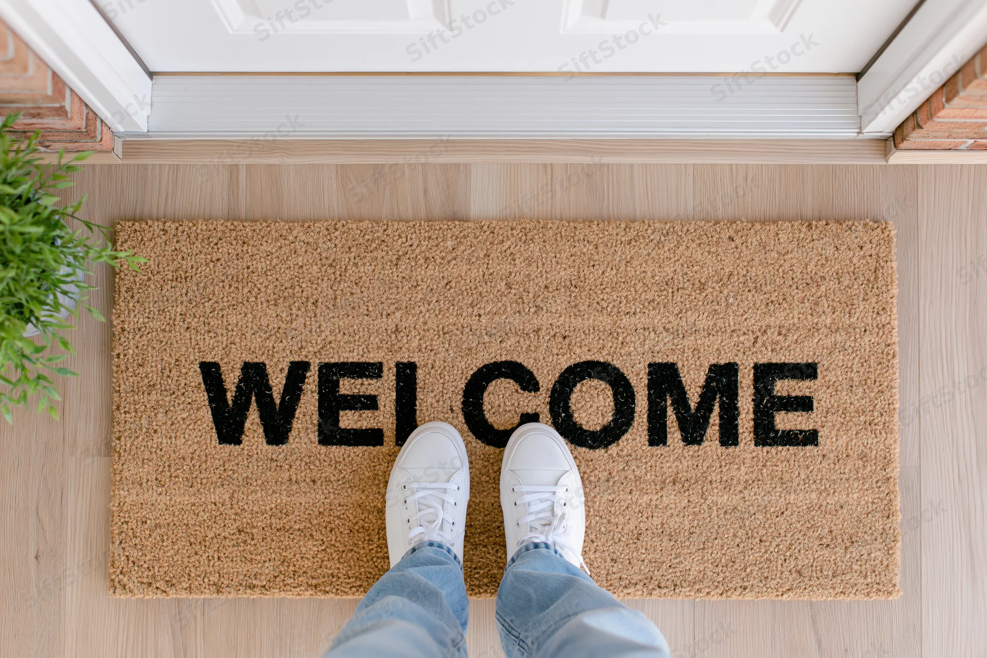 Person standing on welcome doormat at home entrance with white sneakers and jeans