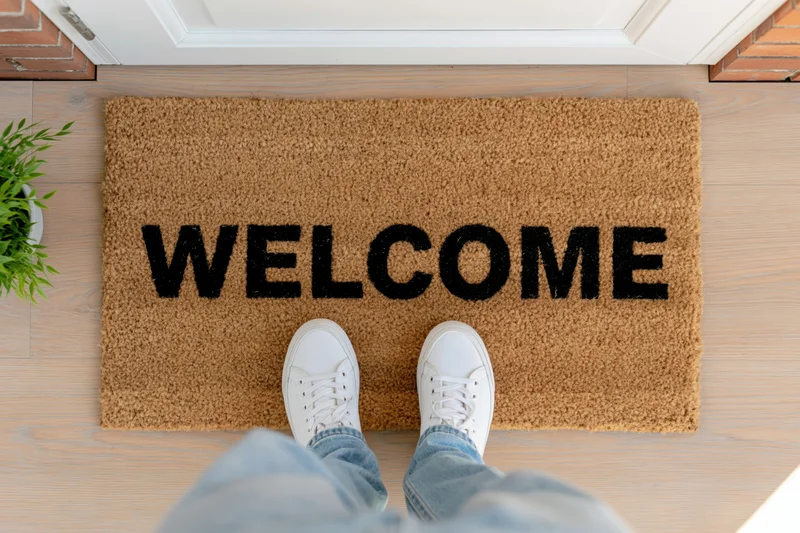 Person standing on welcome doormat at home entrance with white sneakers and jeans