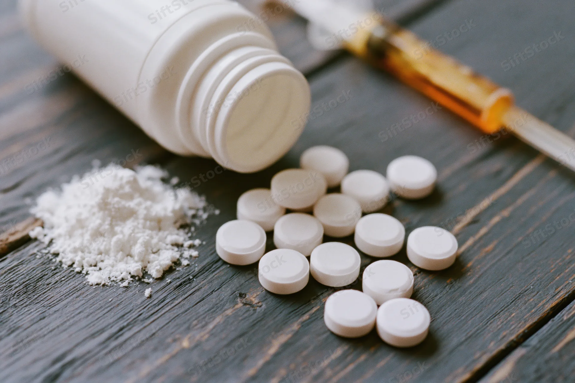 Scattered white pills and powder from an overturned bottle on a dark wooden surface