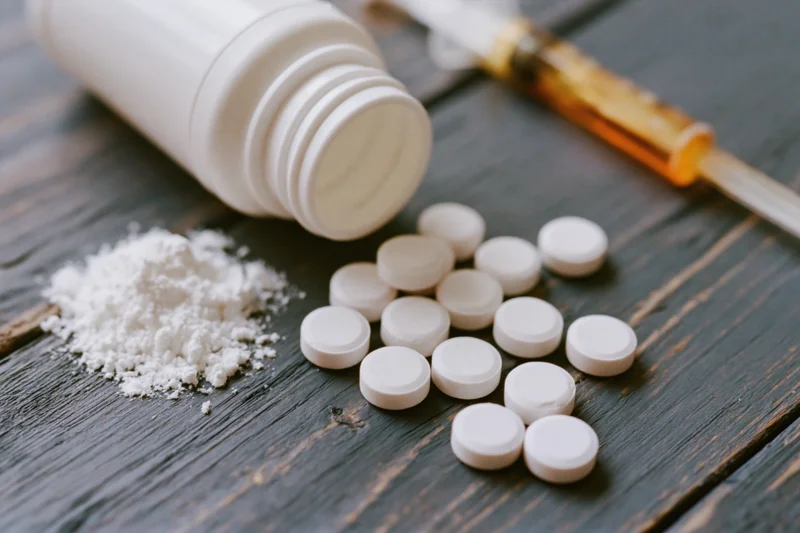 Scattered white pills and powder from an overturned bottle on a dark wooden surface