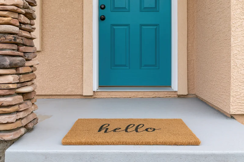 Teal six-panel front door with hello doormat on concrete porch step