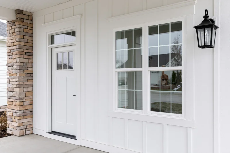 White paneled door on residential home front porch with stone column and black lantern light