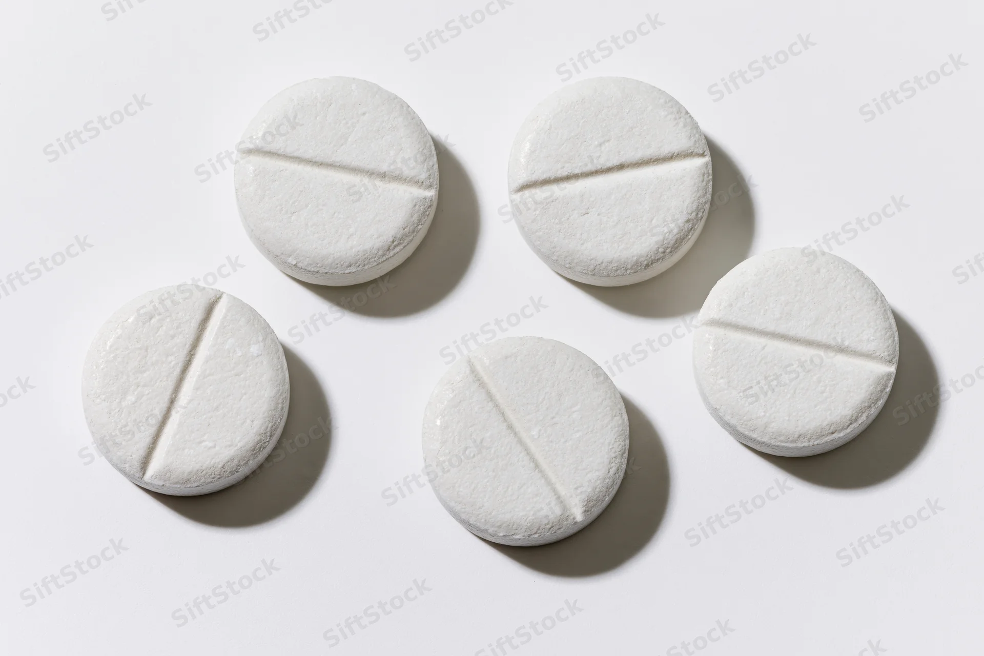 Five white scored tablets arranged in a loose grid on a plain white surface