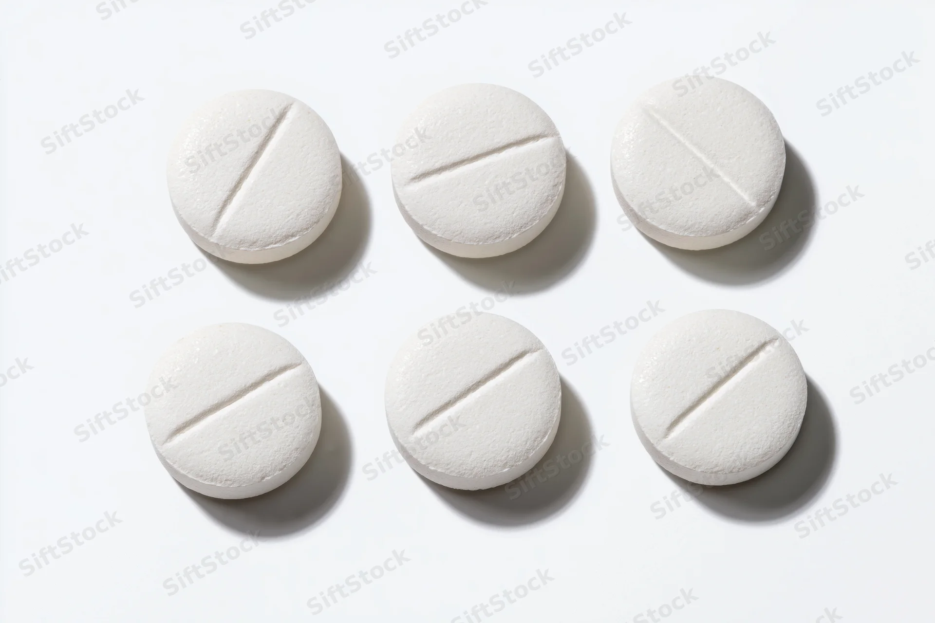 Six white round scored tablets arranged in two rows on a white surface