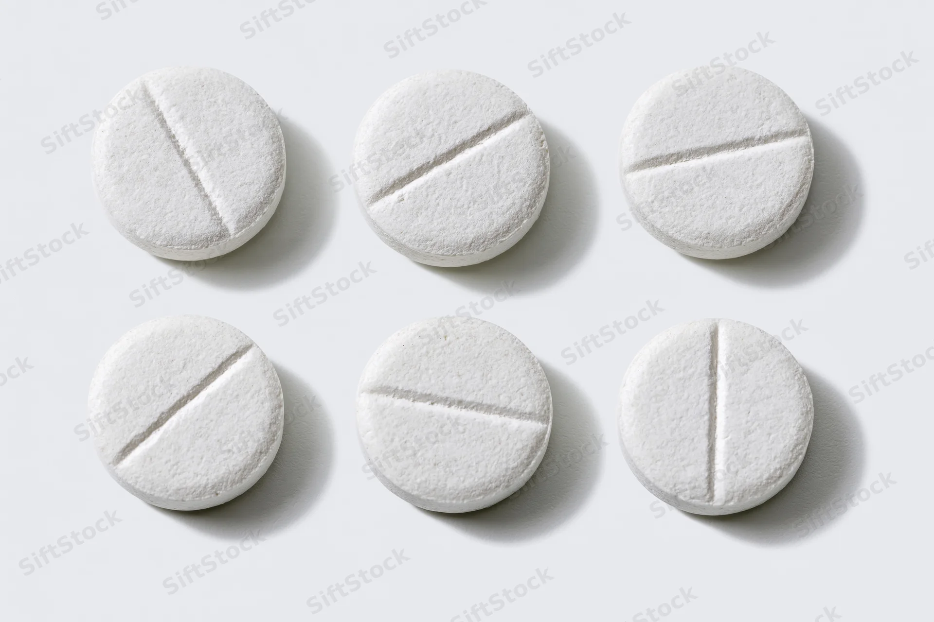 Six white scored tablets arranged in two rows on a plain white surface