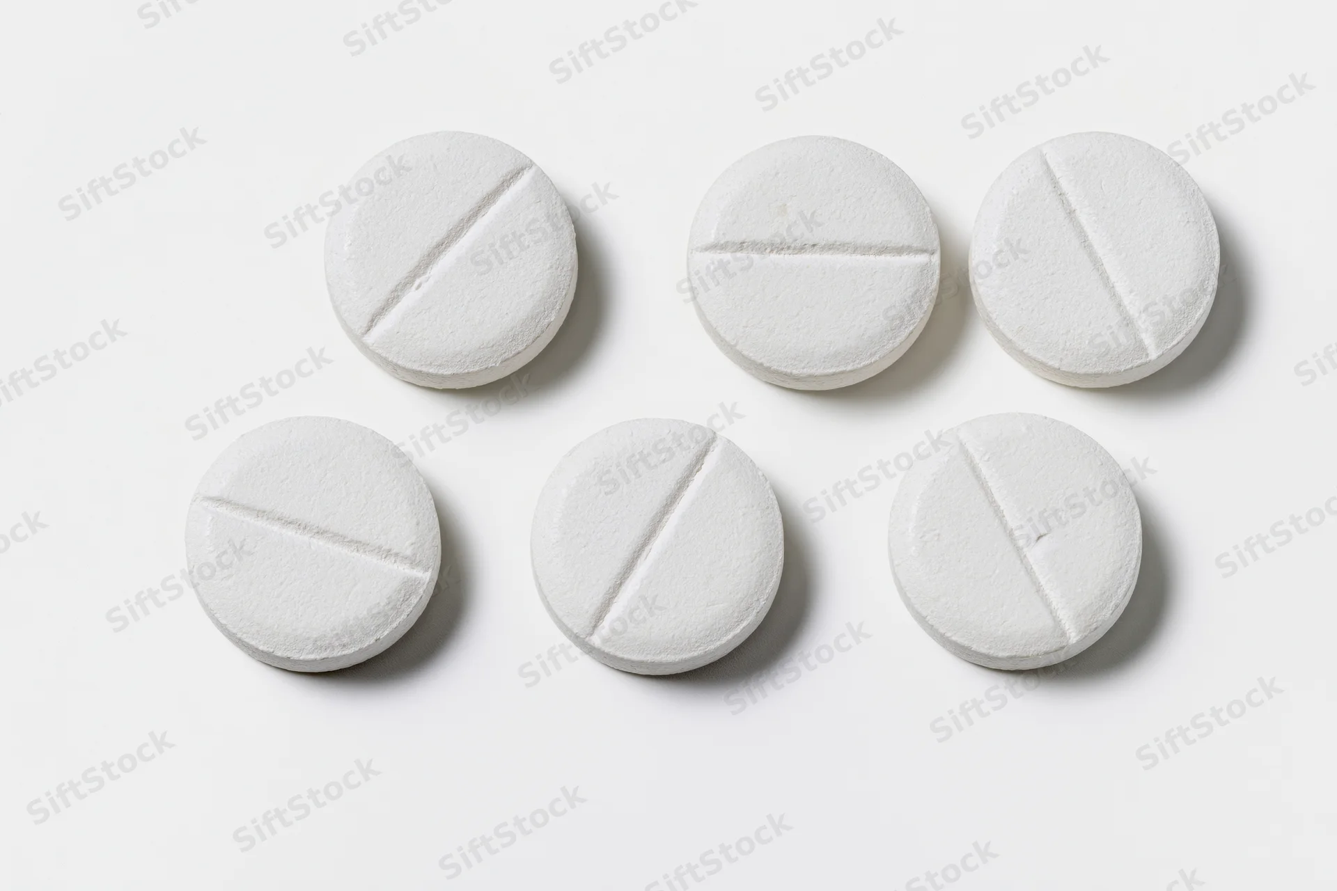 Six white round scored tablets arranged in two rows on a plain white surface
