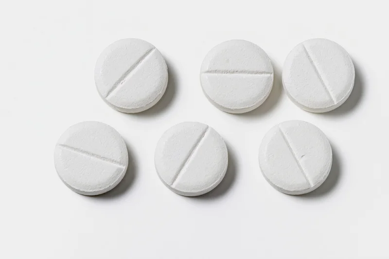 Six white round scored tablets arranged in two rows on a plain white surface