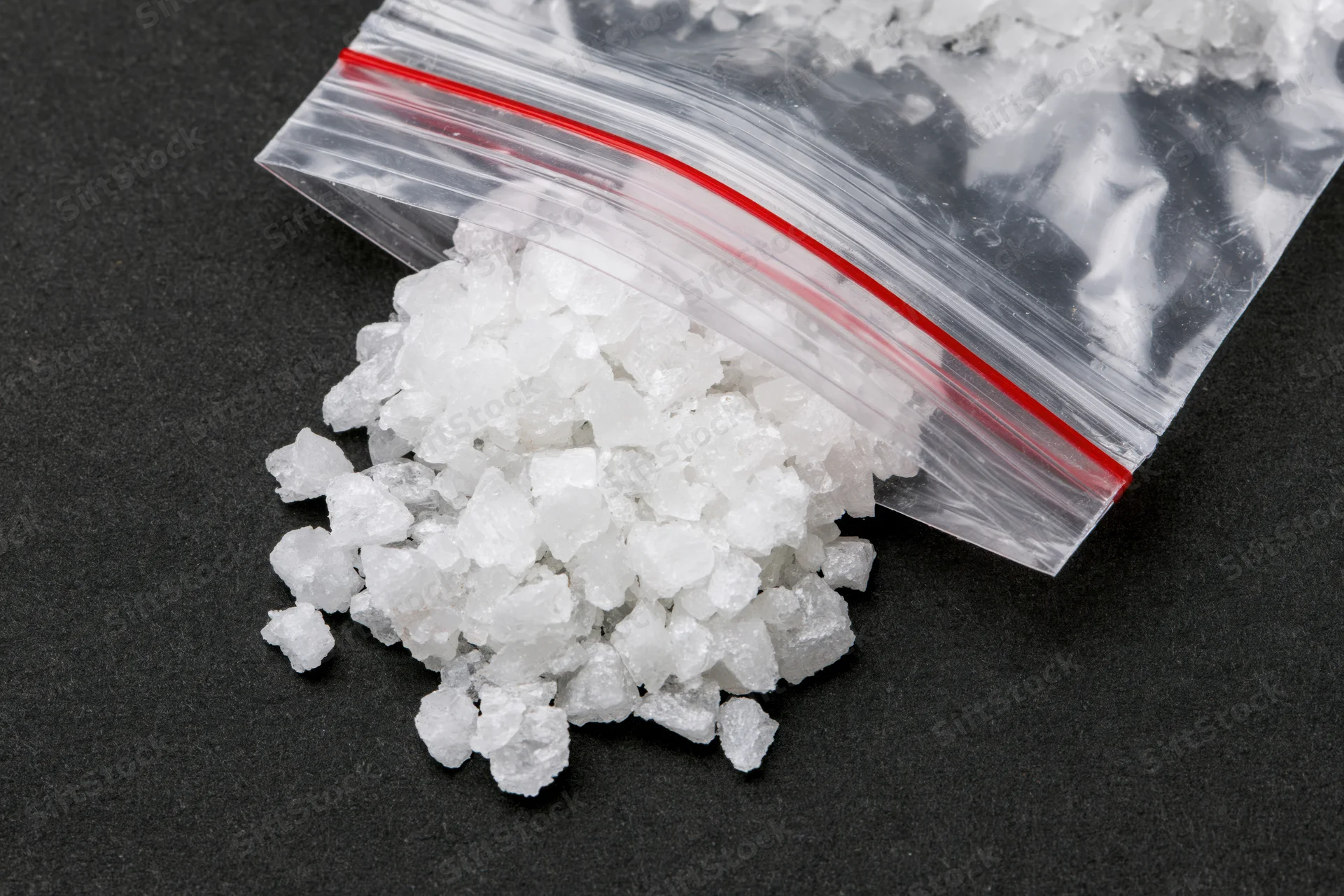 White crystalline mineral spilled from a clear ziplock bag onto a black surface