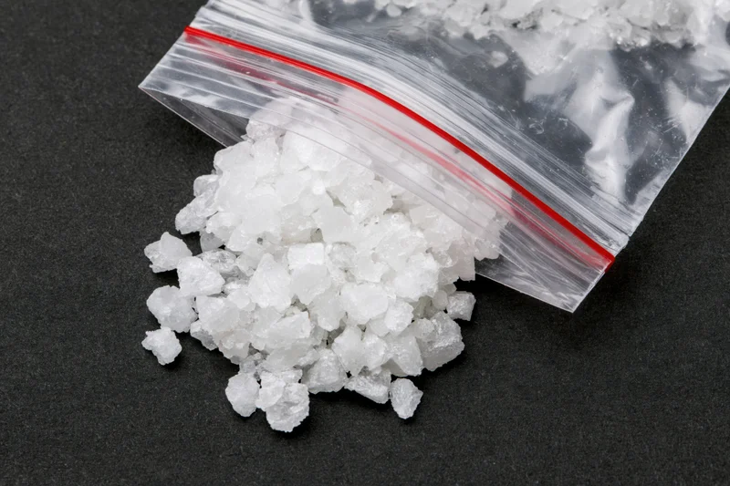 White crystalline mineral spilled from a clear ziplock bag onto a black surface
