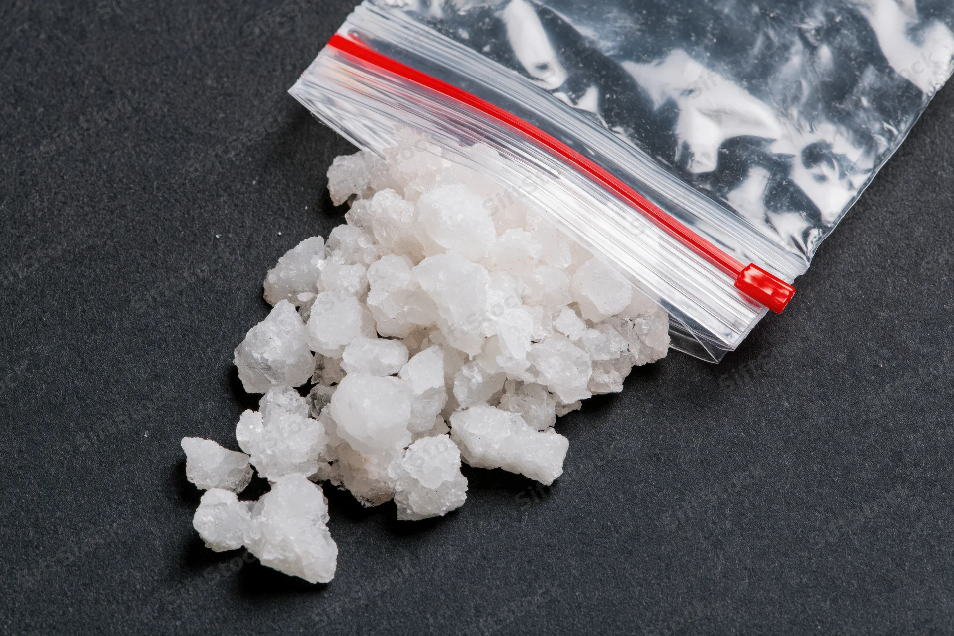 Coarse white salt crystals spilling from a clear resealable plastic bag onto a black surface