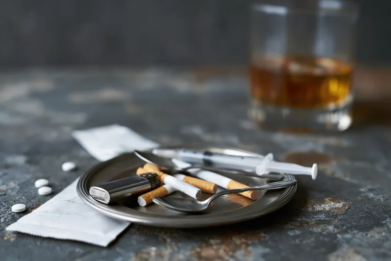 Substance abuse paraphernalia arranged on a dark table with a glass of alcohol in the background