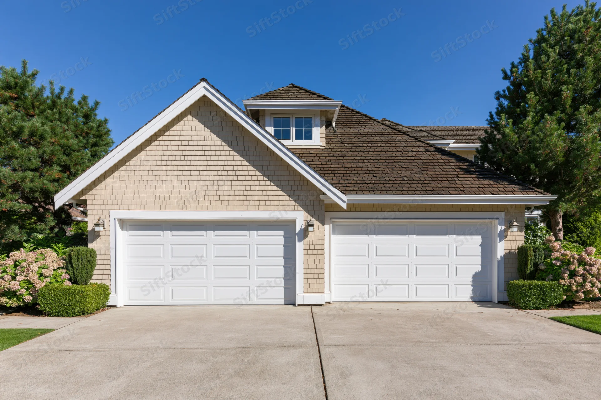 Suburban house exterior with two white raised-panel garage doors and landscaped front yard