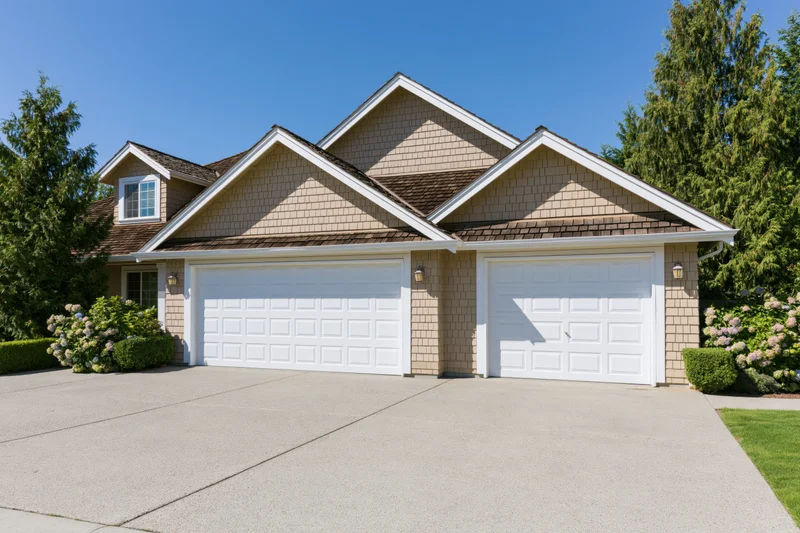 Suburban house exterior with two white raised-panel garage doors and landscaped front yard