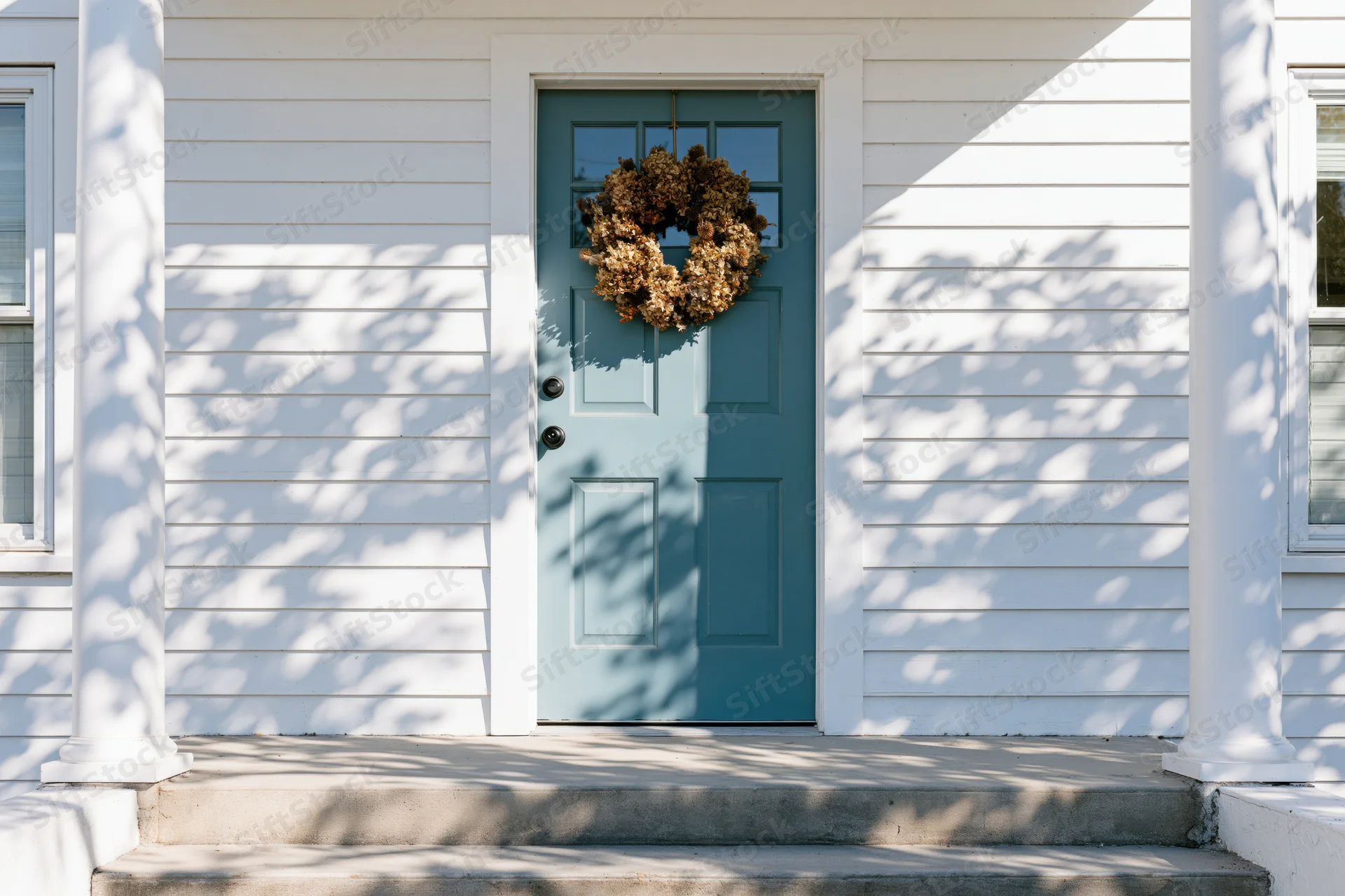 Teal front door with dried hydrangea wreath on white house porch