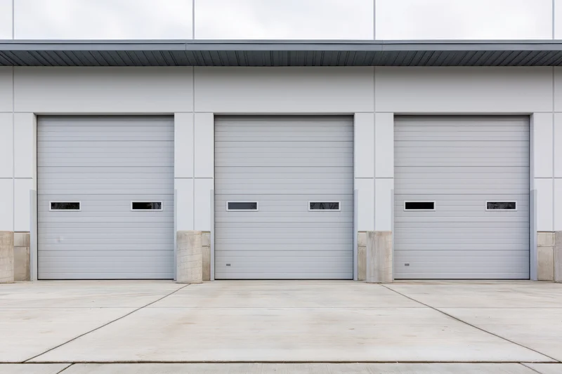Three closed industrial roll-up garage doors on a modern warehouse exterior