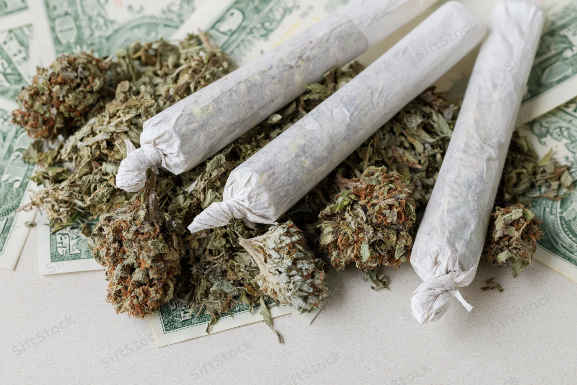 Cannabis buds and rolled joints resting on scattered dollar bills