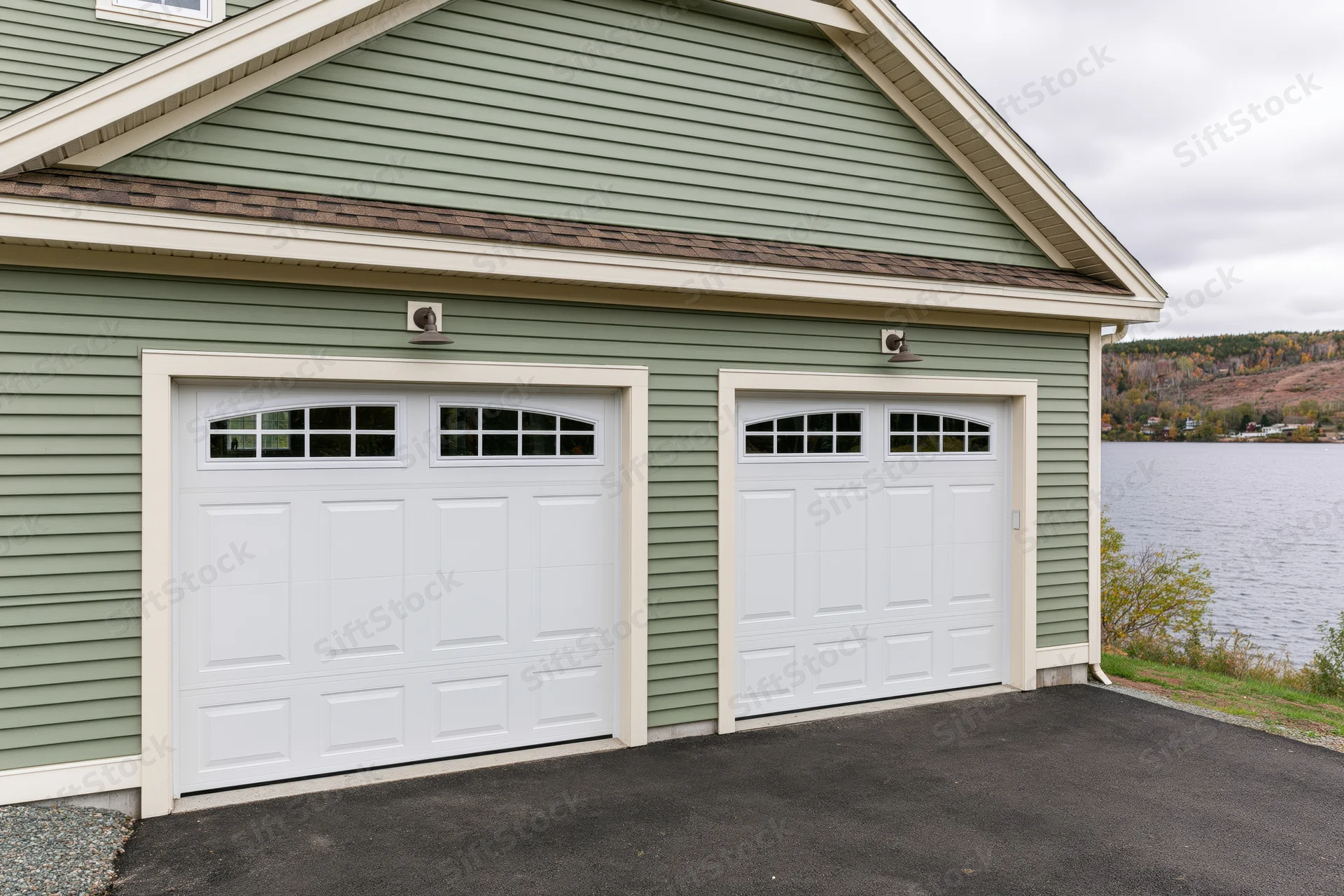 Two-car garage with white doors and sage siding on a lakeside craftsman-style home
