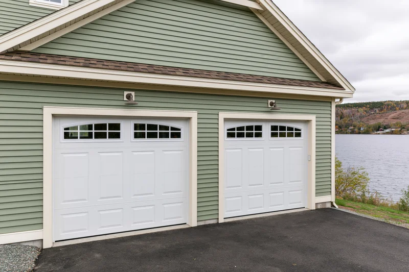 Two-car garage with white doors and sage siding on a lakeside craftsman-style home