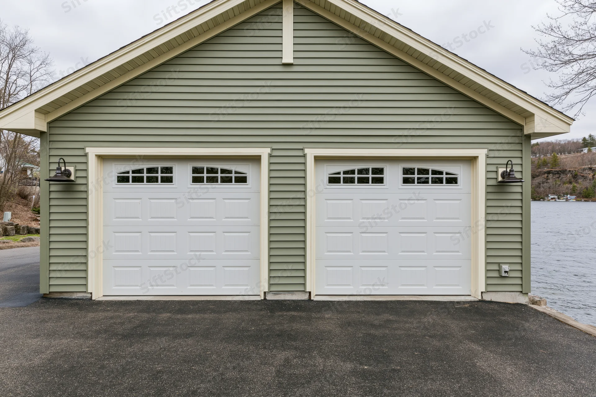 Two-car attached garage with sage siding and white doors on a craftsman-style home by a lake