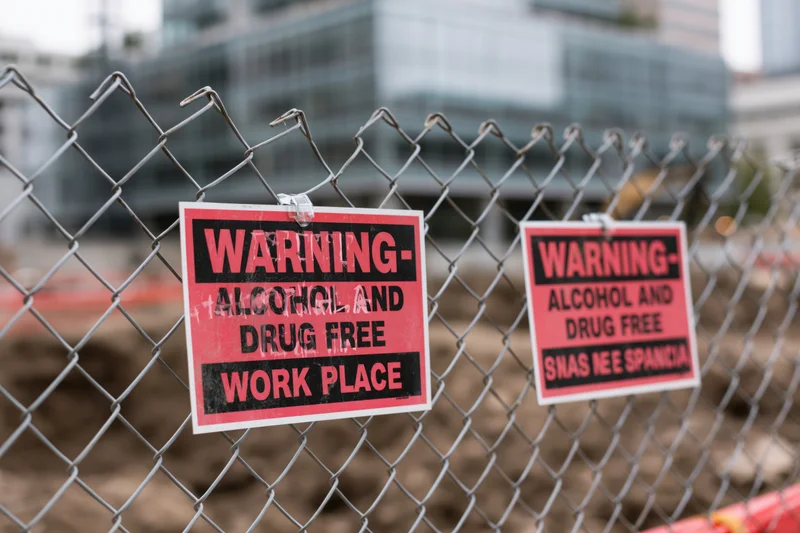 Red and black bilingual warning signs attached to chainlink fence at construction site