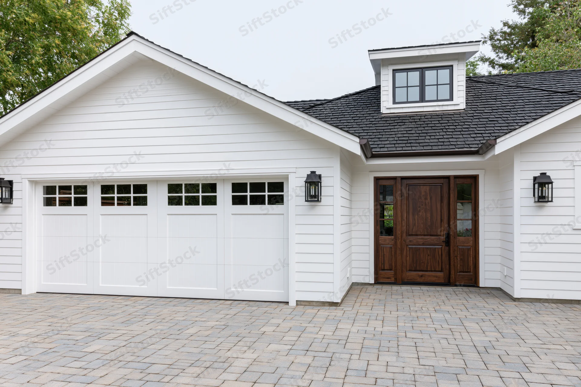 White craftsman-style house exterior with double garage and wooden front door on paved driveway