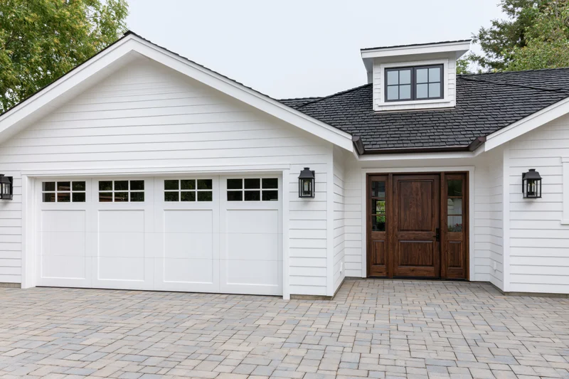 White craftsman-style house exterior with double garage and wooden front door on paved driveway
