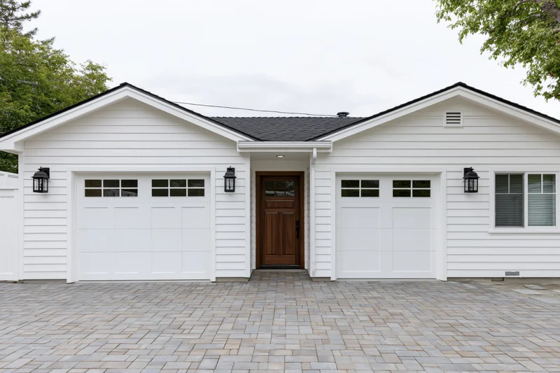 White craftsman-style house exterior with double garages and central front door on paved driveway