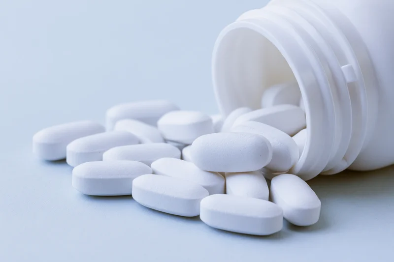 White oval pills spilling from an overturned plastic bottle on a light surface