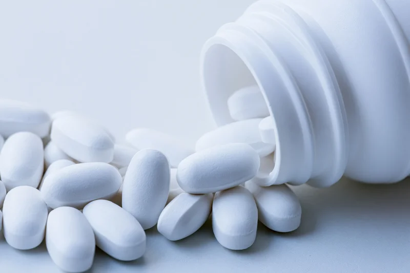 White oval pills spilling from an overturned plastic bottle on a plain surface